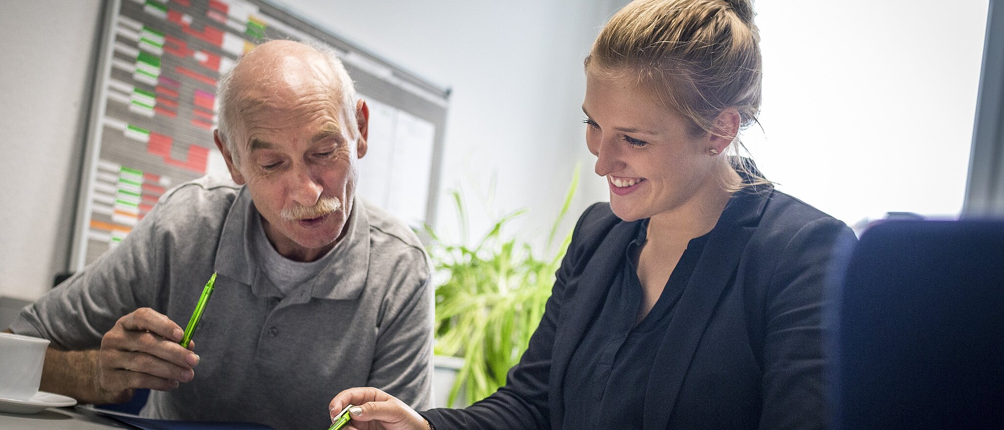 Mitarbeiterin erklärt einem Bewerber am Schreibtisch sitzend verschiedene Beschäftigungsmodelle