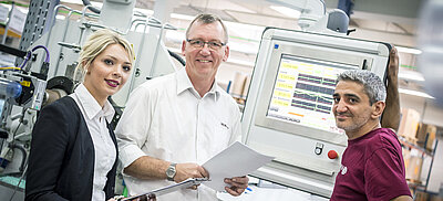 Symbolbild Equal Pay: Mitarbeiter und Führungskräfte stehen in Werkshalle