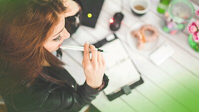 Frau am Schreibtusch mit Stift und Notizbuch