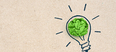 gezeichnete Glühbirne mit zerknülltem grünem Blatt als Symbolbild für Design Thinking