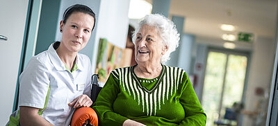 Altenpflegerin mit Bewohnerin im Rollstuhl auf einem Flur